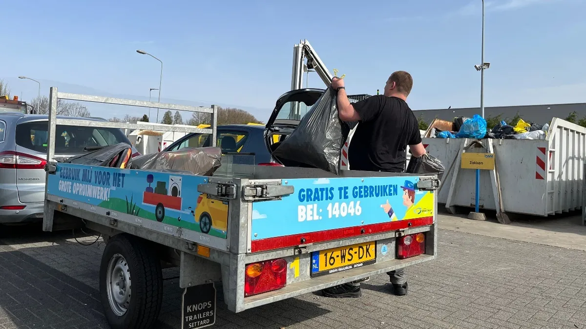 Man op milieupark haalt vuilniszak uit aanhangwagen van De Tuinman